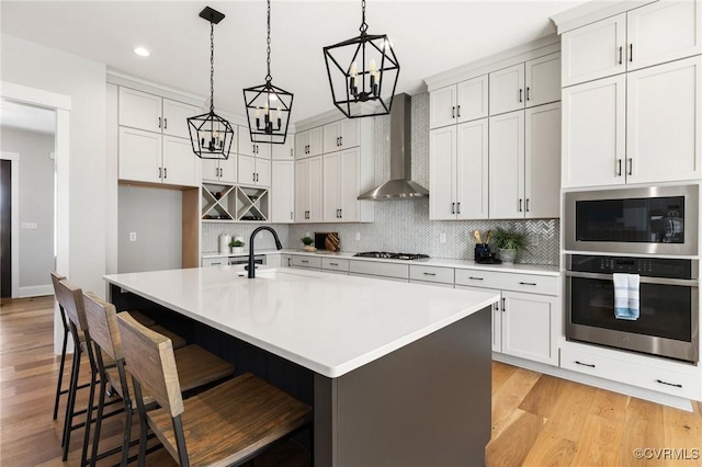 kitchen with gas cooktop, a sink, oven, light countertops, and wall chimney range hood