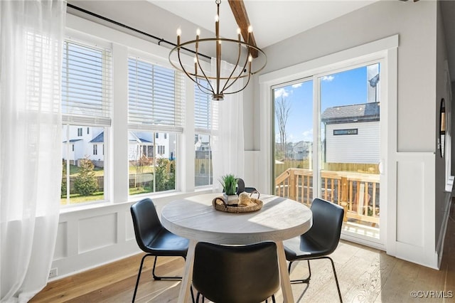 dining space featuring an inviting chandelier, a decorative wall, light wood-style floors, and a wainscoted wall