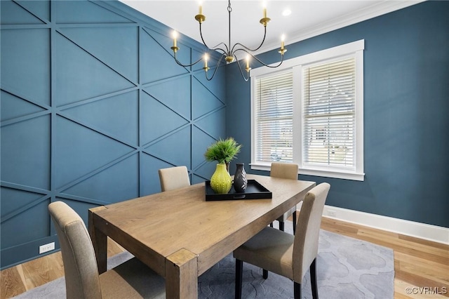 dining area with a decorative wall, baseboards, a notable chandelier, and light wood finished floors