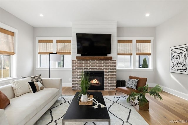 living area with a glass covered fireplace, baseboards, wood finished floors, and recessed lighting