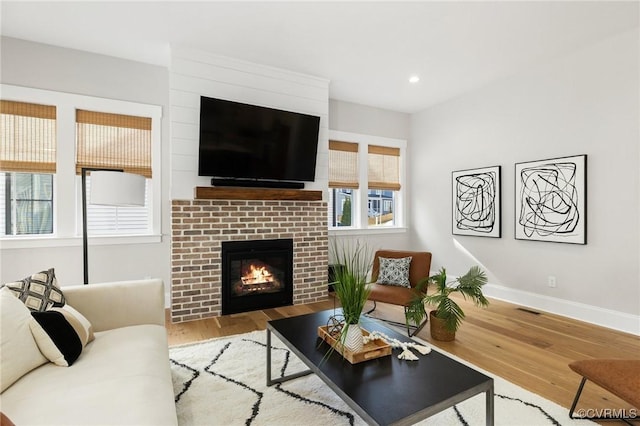 living area featuring visible vents, a brick fireplace, baseboards, recessed lighting, and wood finished floors