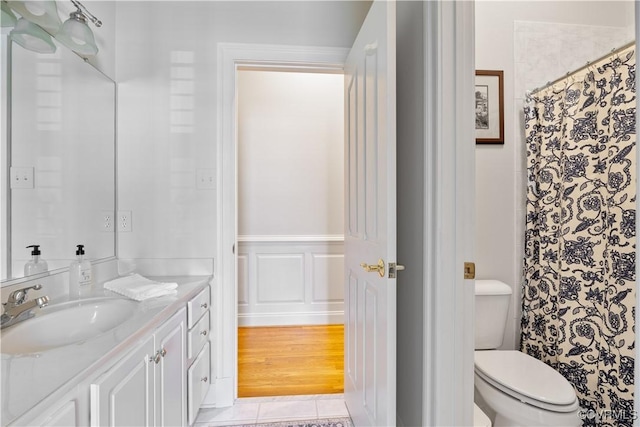 bathroom featuring a wainscoted wall, toilet, a decorative wall, tile patterned flooring, and vanity