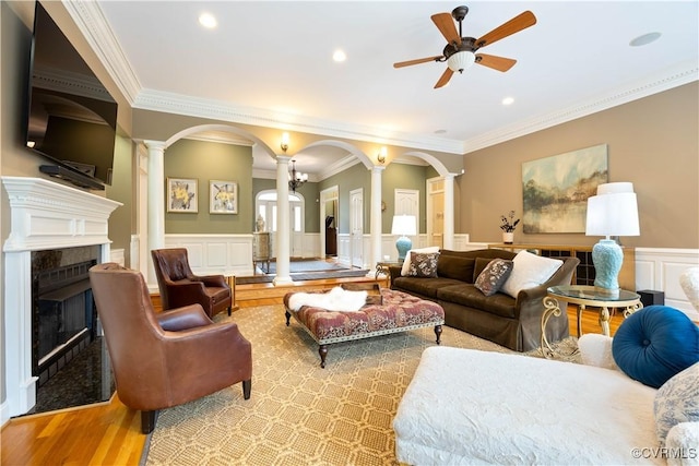 living area featuring arched walkways, wood finished floors, ceiling fan, and decorative columns