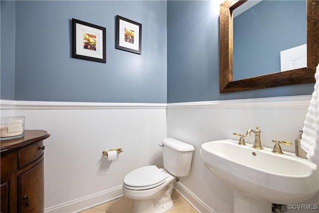 half bathroom featuring a sink, baseboards, toilet, and tile patterned flooring