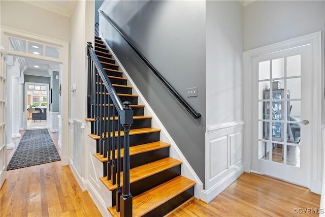 staircase featuring wainscoting, wood finished floors, crown molding, and a decorative wall