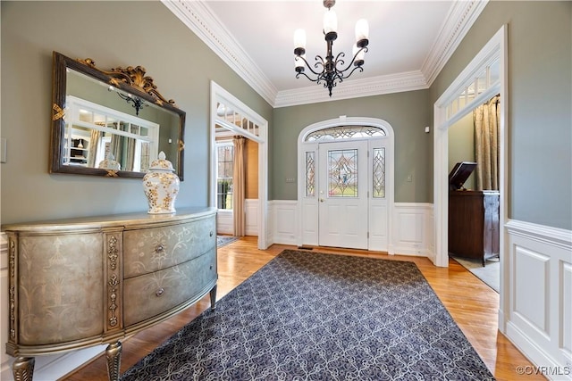 foyer entrance featuring a wainscoted wall, a notable chandelier, wood finished floors, and crown molding