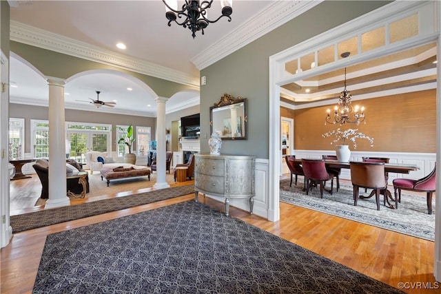 living area with wood finished floors, arched walkways, wainscoting, crown molding, and decorative columns