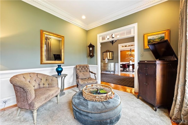 sitting room featuring crown molding, wood finished floors, a chandelier, and wainscoting