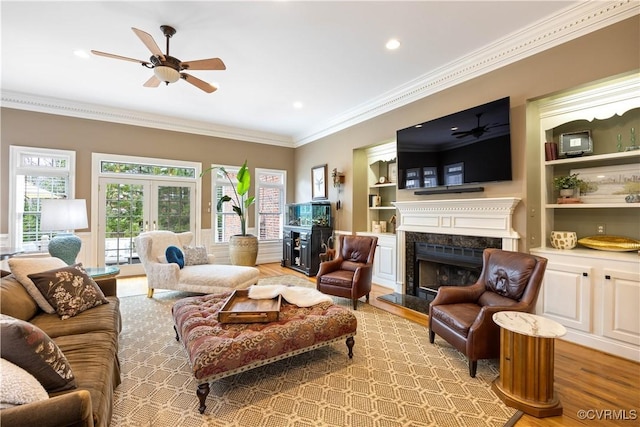 living room featuring a ceiling fan, built in features, wood finished floors, a high end fireplace, and crown molding