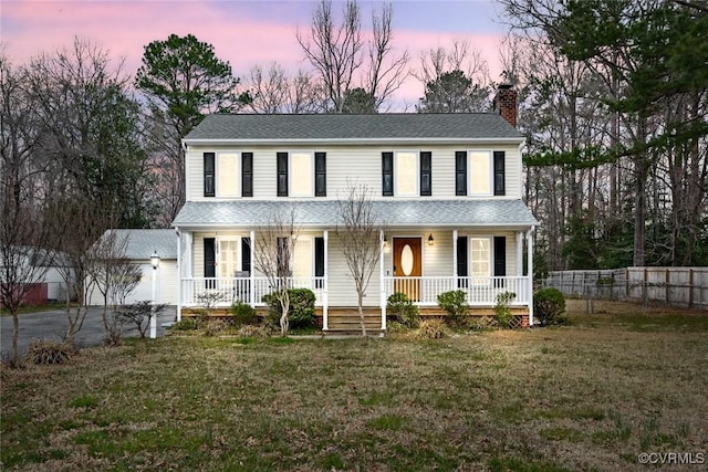 view of front of house featuring an outbuilding, a front lawn, fence, covered porch, and a chimney