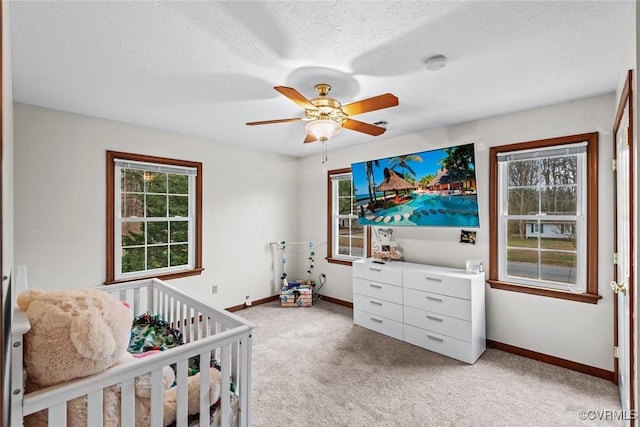 bedroom with a ceiling fan, a textured ceiling, a nursery area, baseboards, and light colored carpet