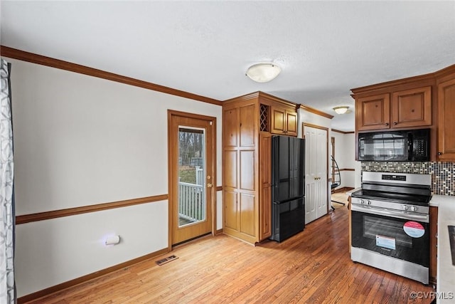 kitchen featuring tasteful backsplash, visible vents, light wood-type flooring, ornamental molding, and black appliances