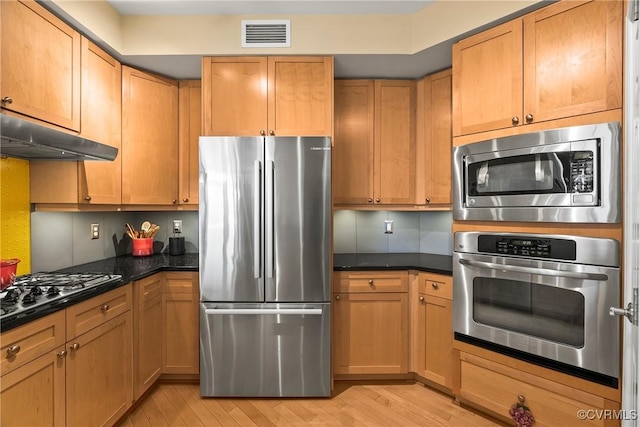 kitchen featuring visible vents, under cabinet range hood, light wood-style flooring, appliances with stainless steel finishes, and dark stone countertops