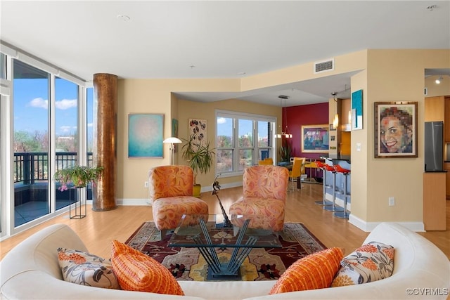 living area with a wall of windows, wood finished floors, visible vents, and baseboards