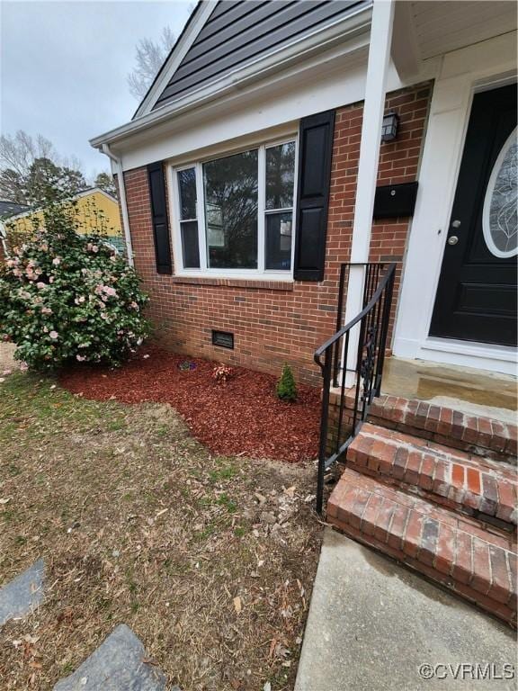 view of exterior entry with brick siding and crawl space