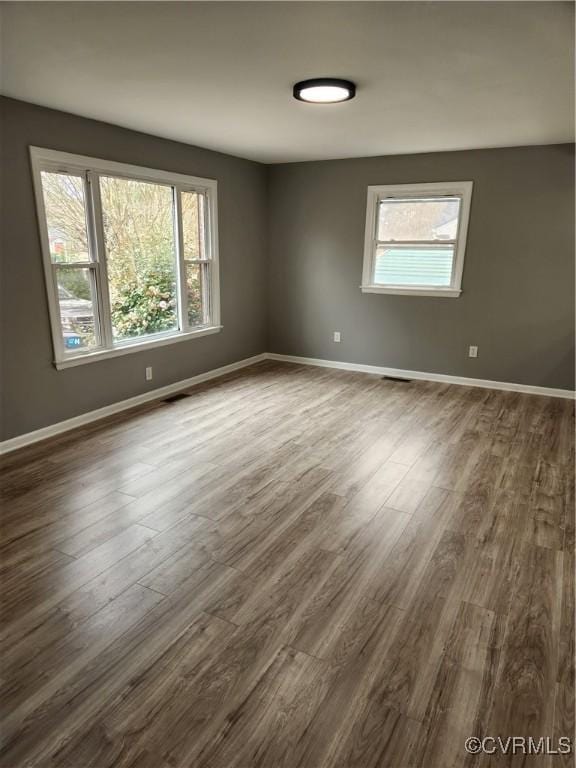 unfurnished room with visible vents, baseboards, and dark wood-type flooring