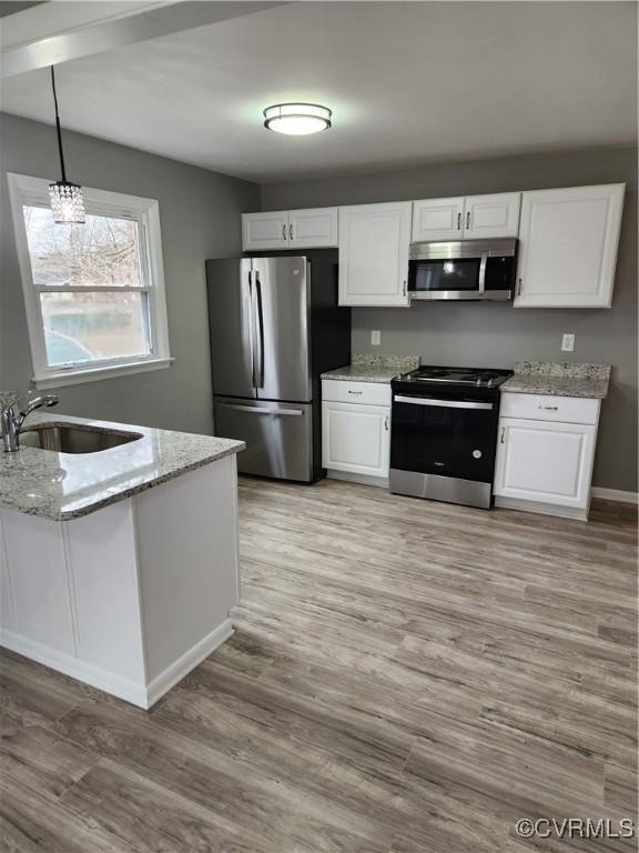 kitchen with light stone counters, light wood-style flooring, a sink, stainless steel appliances, and white cabinetry