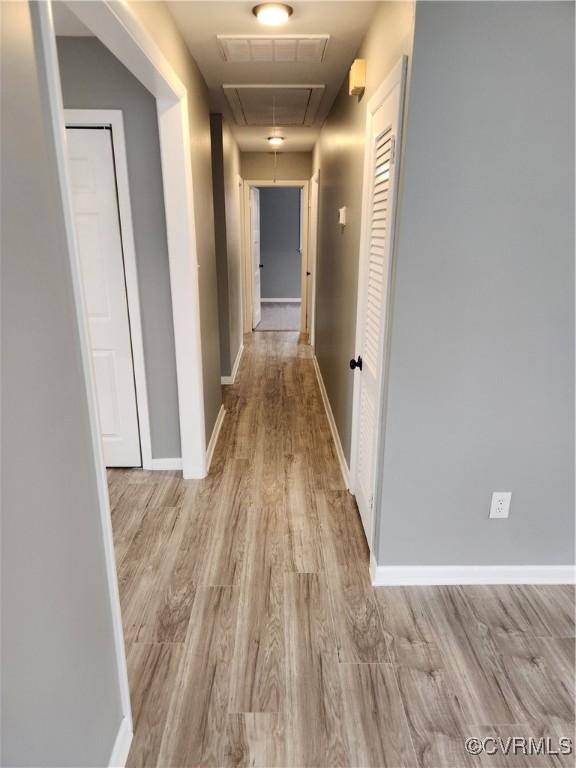 corridor featuring visible vents, baseboards, attic access, and light wood-style flooring