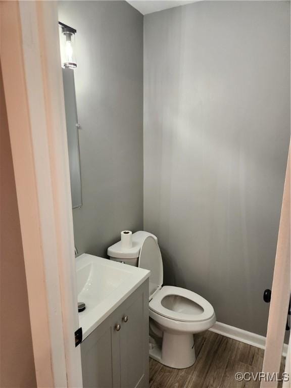 bathroom featuring baseboards, toilet, wood finished floors, and vanity