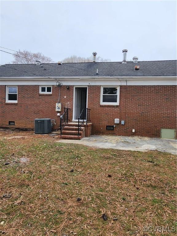 rear view of house with a lawn, a patio, crawl space, brick siding, and central AC unit