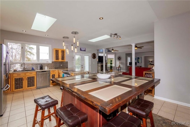 kitchen with a kitchen bar, backsplash, stainless steel appliances, a skylight, and light tile patterned flooring