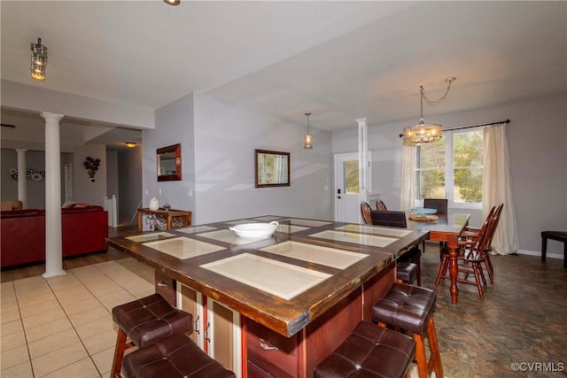 tiled dining area featuring baseboards, a chandelier, and ornate columns