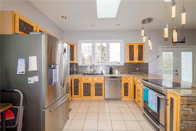 kitchen featuring backsplash, glass insert cabinets, a peninsula, stainless steel appliances, and a sink