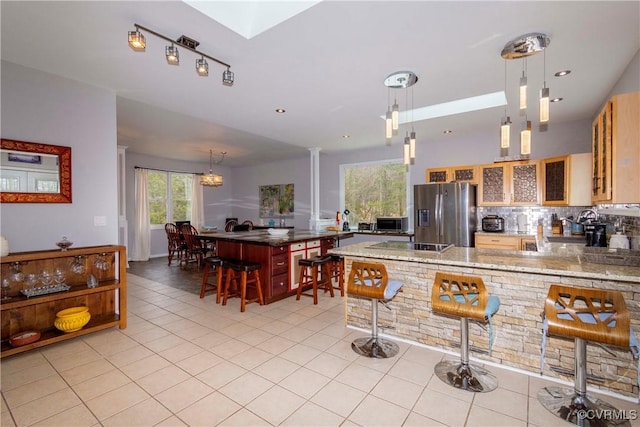 kitchen featuring light tile patterned floors, ornate columns, a peninsula, decorative backsplash, and appliances with stainless steel finishes