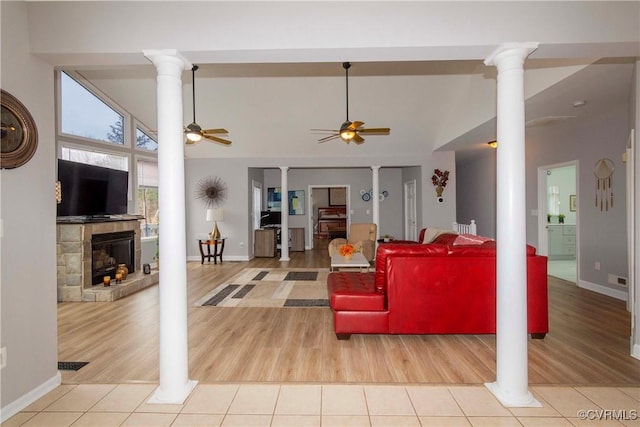 living room featuring light tile patterned floors, high vaulted ceiling, decorative columns, a fireplace with raised hearth, and ceiling fan