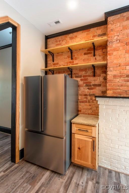 kitchen with wood finished floors, visible vents, brick wall, open shelves, and freestanding refrigerator