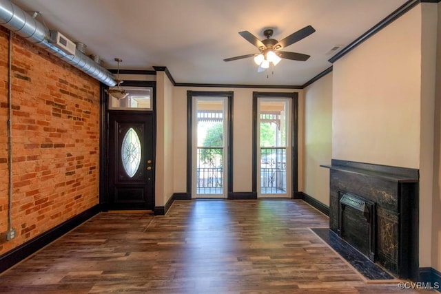 foyer entrance with a fireplace with flush hearth, brick wall, ceiling fan, and wood finished floors