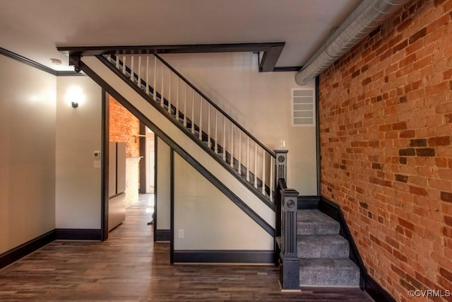 stairway featuring visible vents, brick wall, baseboards, ornamental molding, and wood finished floors