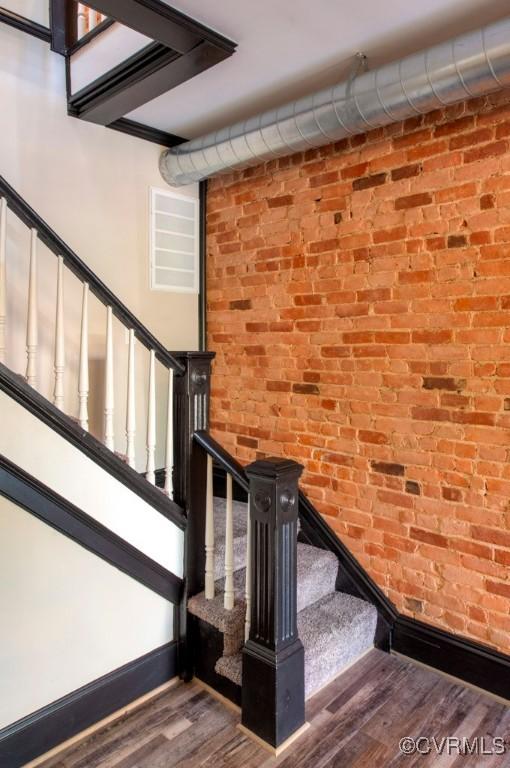 stairs with wood finished floors, baseboards, and brick wall