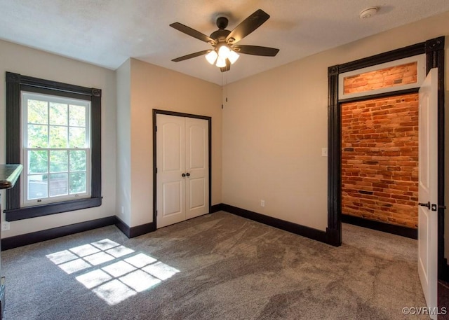 unfurnished bedroom featuring baseboards, carpet floors, ceiling fan, and brick wall