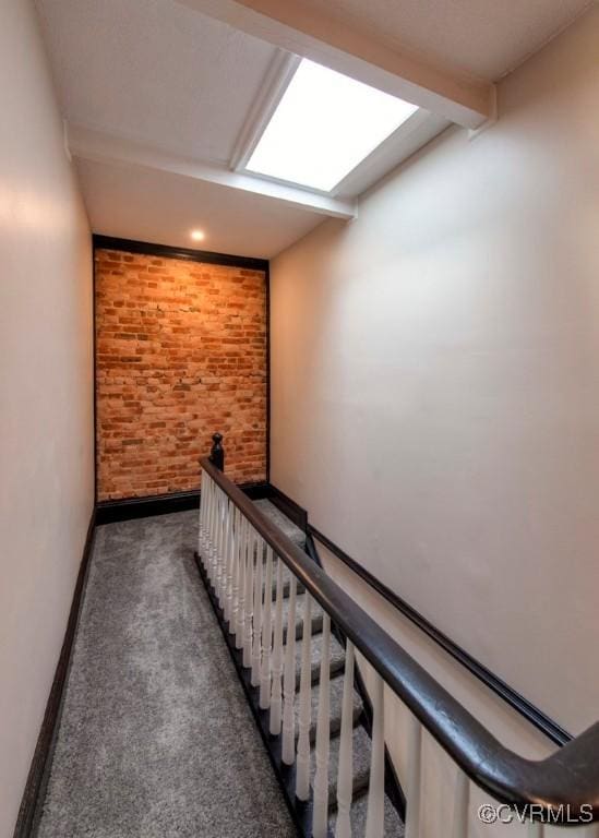 stairs with beam ceiling, carpet, baseboards, and brick wall