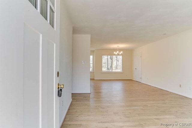 empty room featuring a chandelier, baseboards, and light wood-style floors