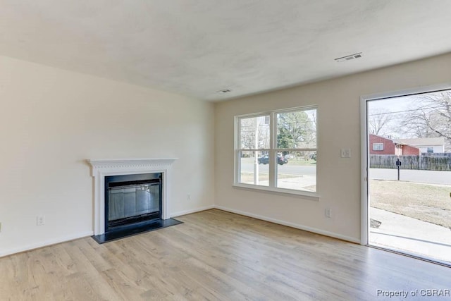 unfurnished living room with a glass covered fireplace, wood finished floors, a healthy amount of sunlight, and visible vents