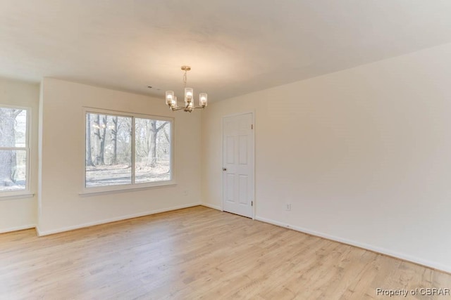 unfurnished room featuring light wood finished floors, a notable chandelier, and plenty of natural light