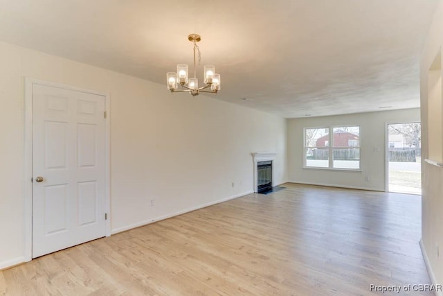 unfurnished living room featuring baseboards, a fireplace with flush hearth, a notable chandelier, and light wood finished floors