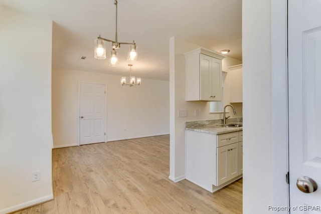 kitchen with a sink, light wood-type flooring, a chandelier, and white cabinetry