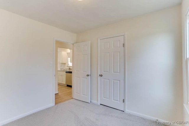 unfurnished bedroom with a sink, baseboards, and light carpet