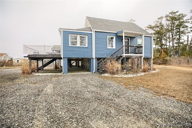 coastal inspired home with roof with shingles, gravel driveway, covered porch, stairs, and a carport