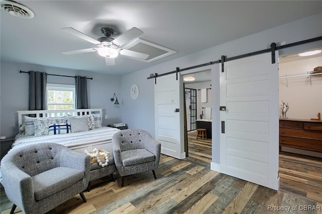 bedroom with visible vents, ceiling fan, a barn door, and wood finished floors