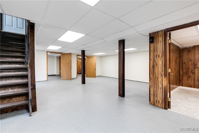 finished basement with a drop ceiling, wooden walls, and stairs