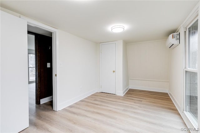 empty room featuring baseboards, light wood-style flooring, and a wall mounted AC