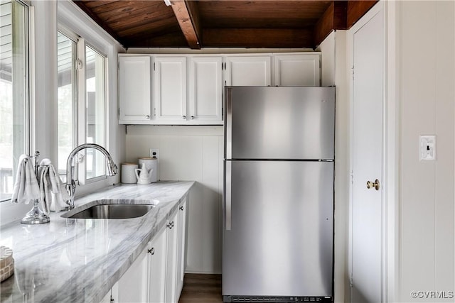 kitchen with a sink, light stone counters, white cabinetry, freestanding refrigerator, and wood ceiling