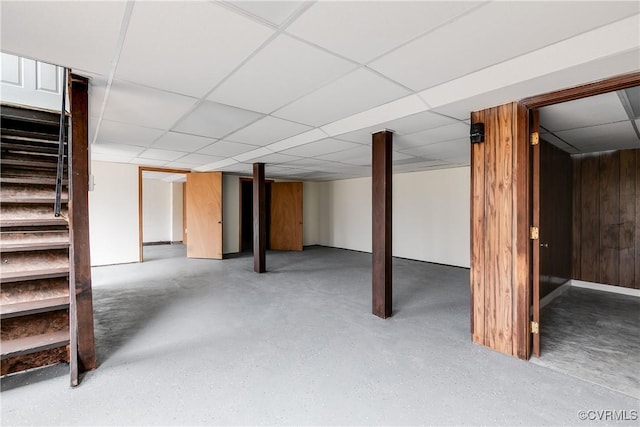 finished basement with stairway, wooden walls, and a paneled ceiling