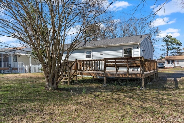 rear view of house featuring a wooden deck, a yard, and roof with shingles