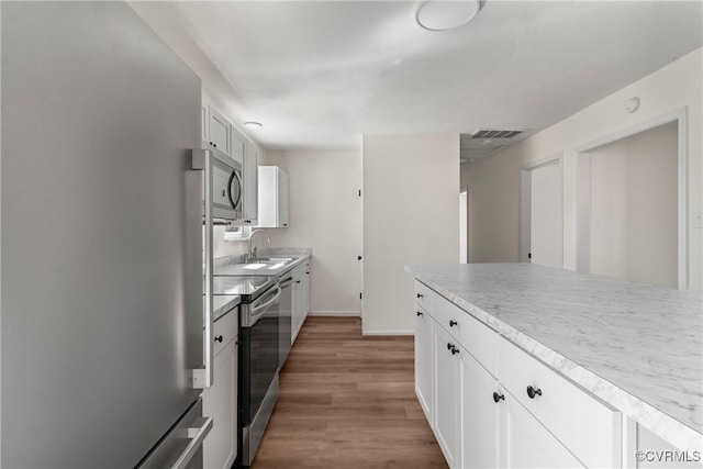 kitchen with visible vents, light wood finished floors, a sink, white cabinets, and appliances with stainless steel finishes