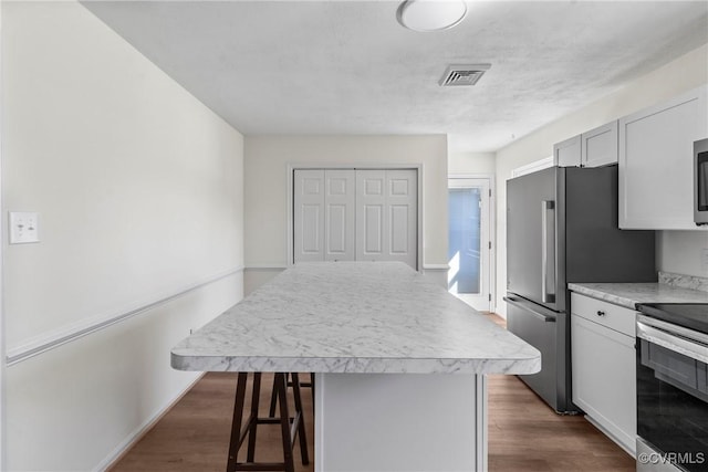 kitchen featuring a center island, a breakfast bar, light countertops, appliances with stainless steel finishes, and dark wood-style floors